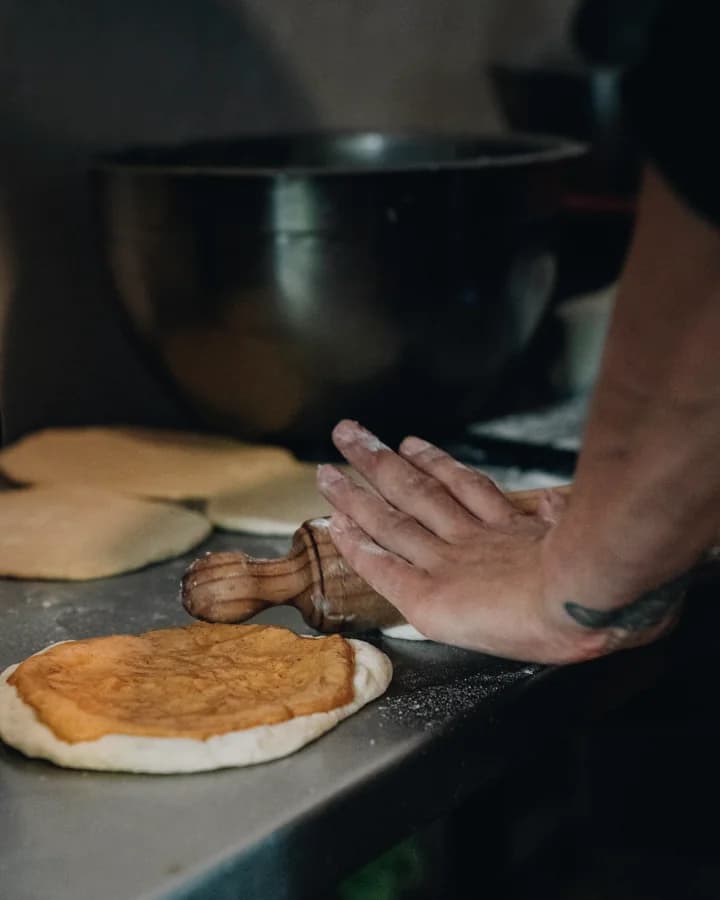 Hands roll dough on a worktable.